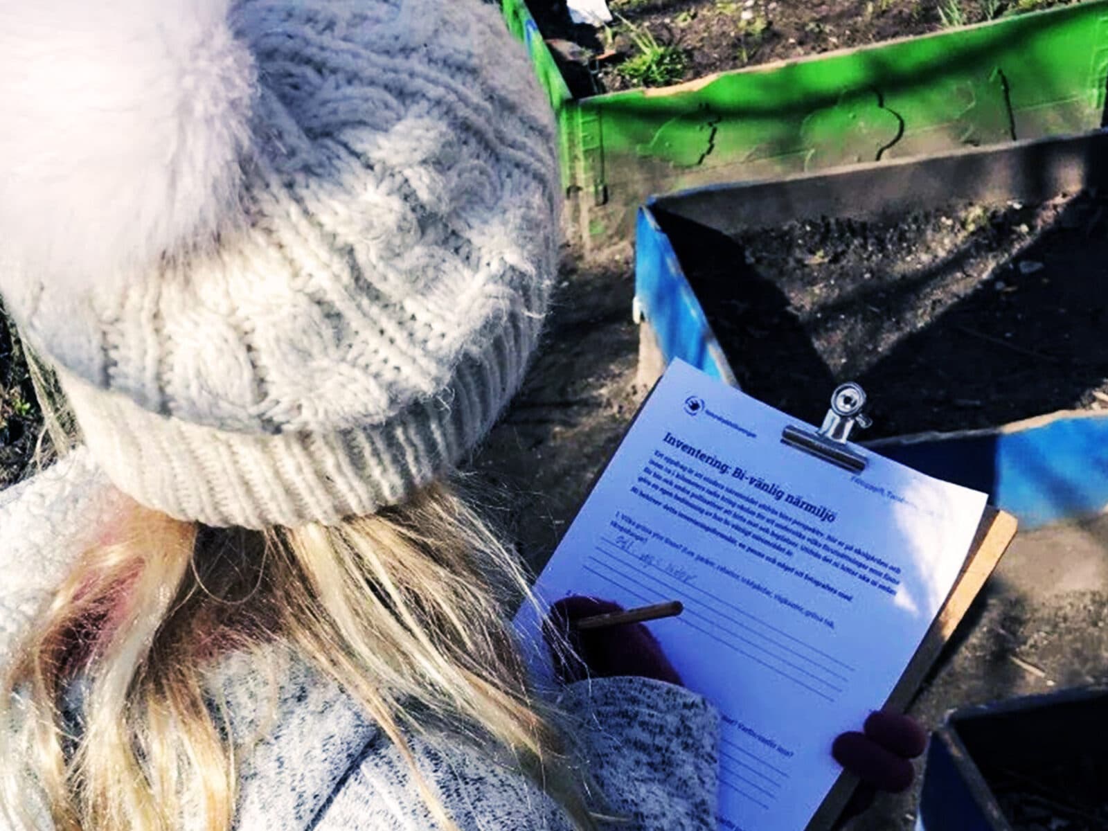 En elev med ett formulär i handen framför odlingslådor