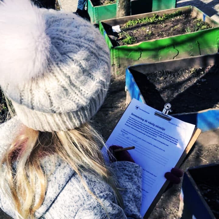 En elev med ett formulär i handen framför odlingslådor